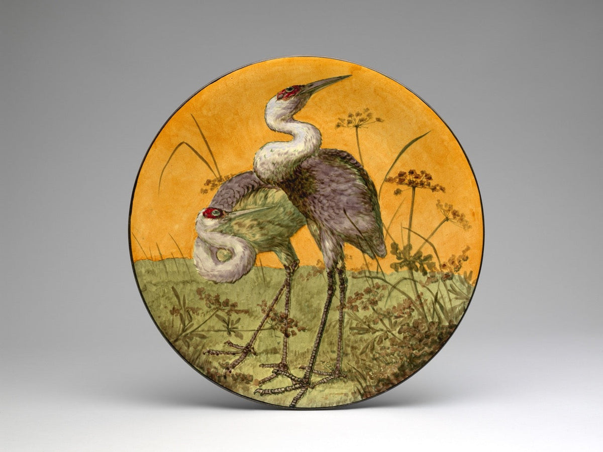 Hand-painted plate showcasing two cranes in a marshy landscape against an orange backdrop, evoking a tranquil, nature-inspired aesthetic.

