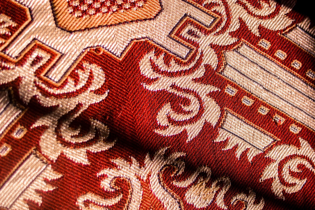 Intricate, antique-inspired textiles in rich reds, golds, and creams, featuring ornate patterns and vintage elegance.
