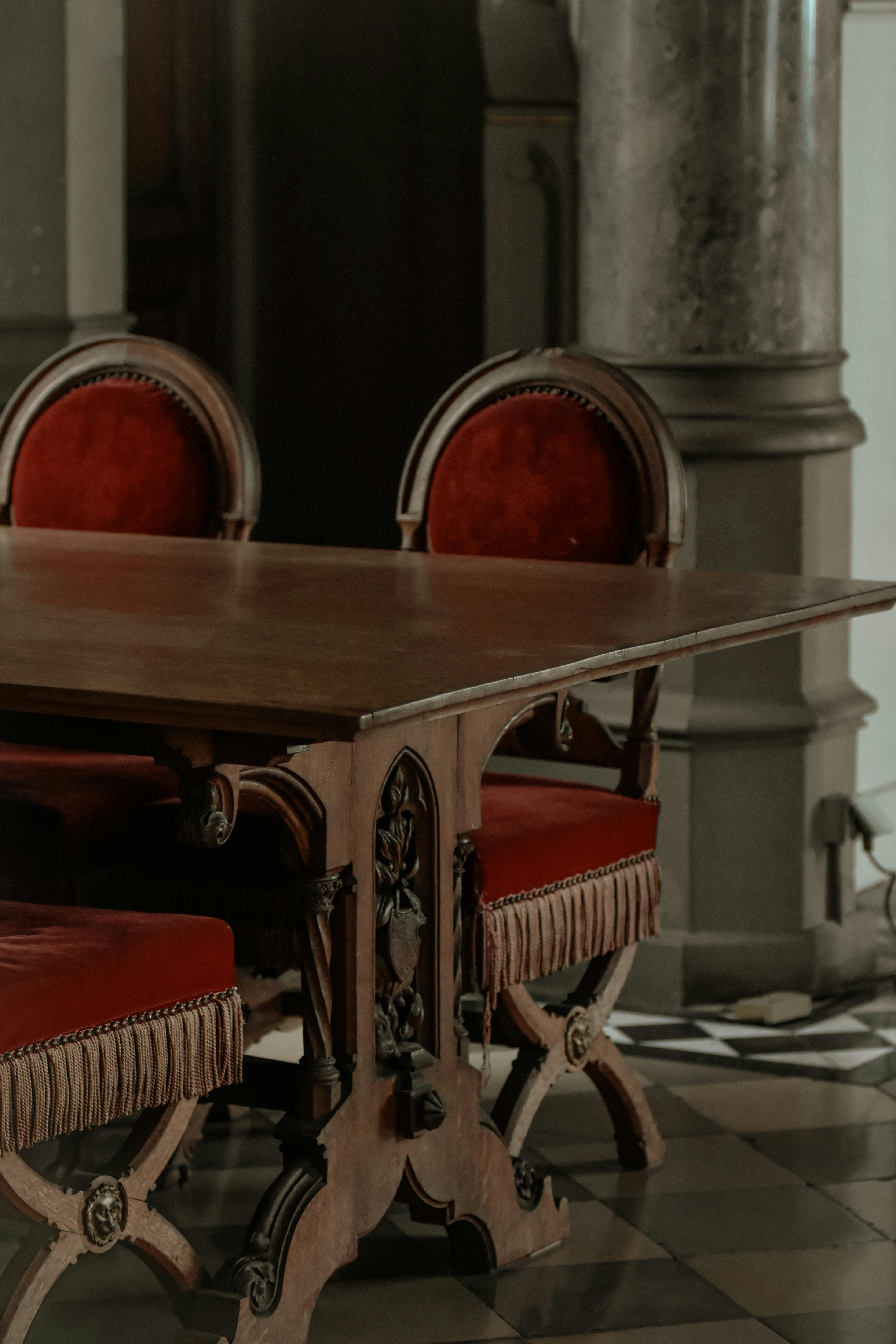 Elegantly carved wooden chairs and table showcase the dark wood tones and rich red velvet of antique furniture.
