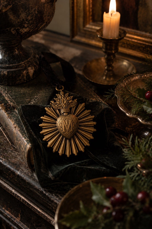 Gold-coloured Sacred Heart ornament resting on dark fabric beside a lit candle.