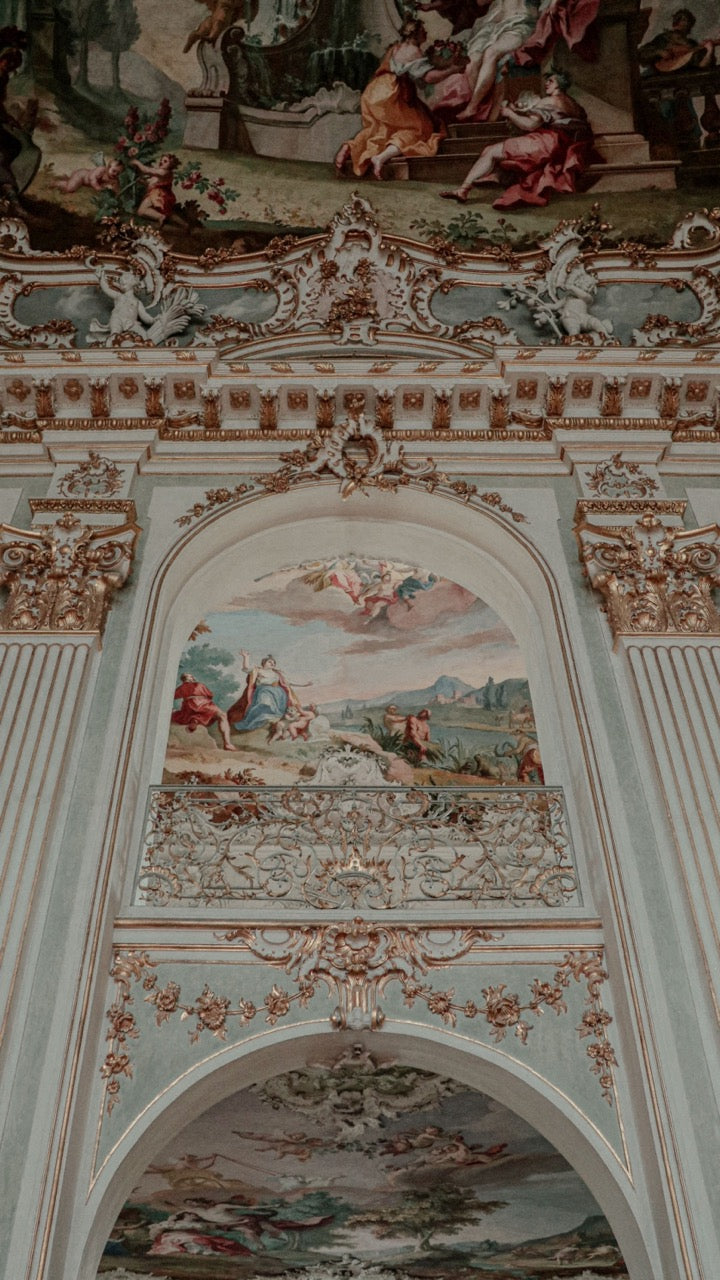 Pastel-painted ornate interior with decorative arches, gilding and ceiling frescoes.