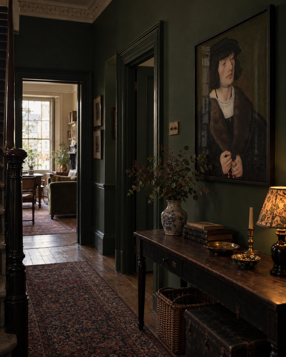 Classical male portrait above a wooden console in a dark green hallway.