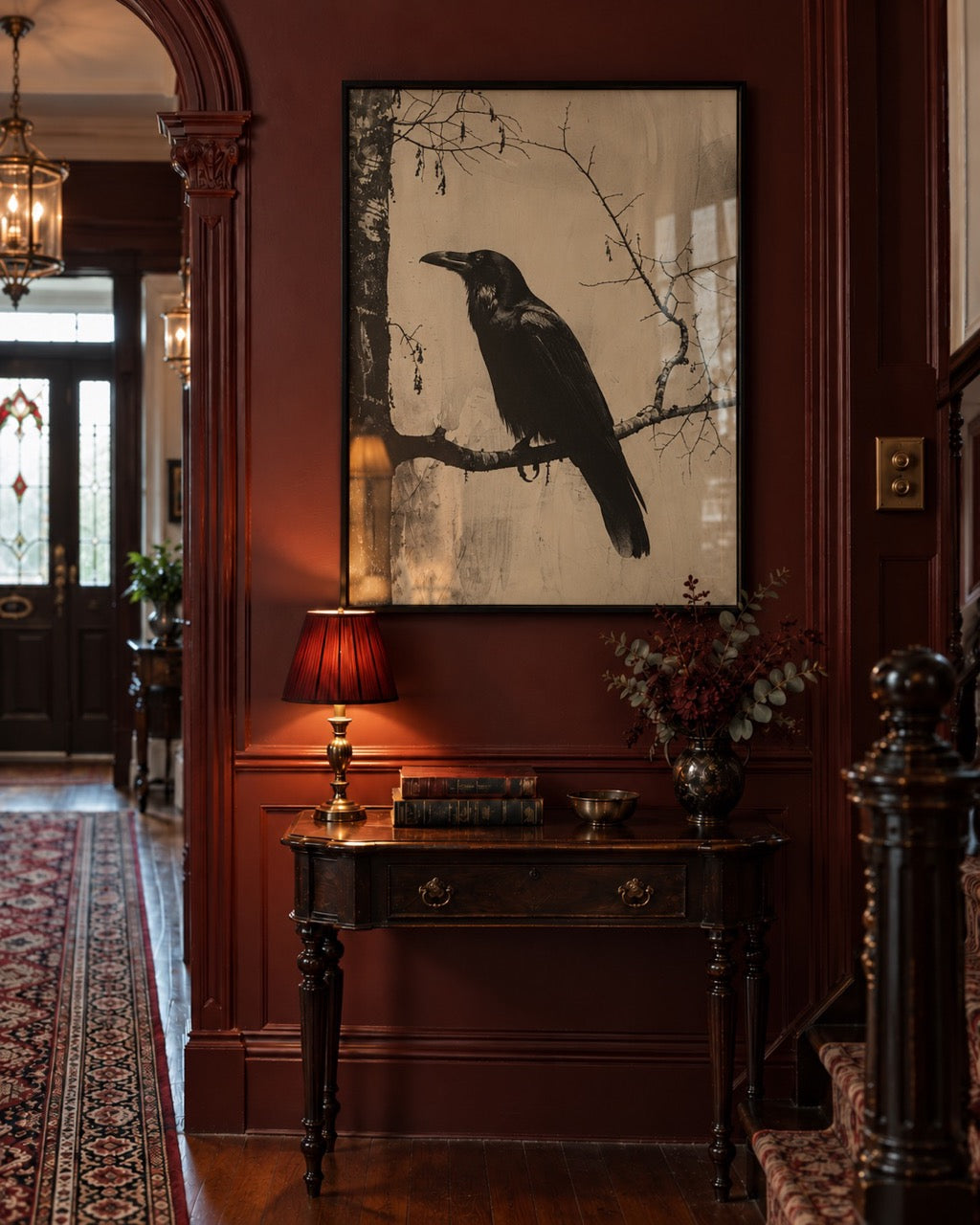 Framed black bird illustration above a wooden chest in a burgundy hallway.