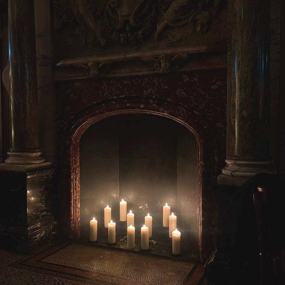 Dimly lit marble fireplace with a dark arch, lit by ten glowing white candles on the mosaic floor.